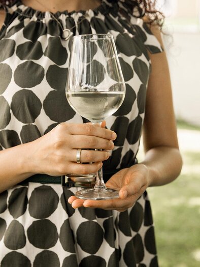 A woman is holding a wine glass in her hand while wearing a polka-dotted dress. In the background, there is a green lawn. | © Weinbauverein