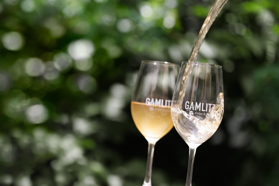Zwei Gläser mit dem Aufdruck "GAMLIT", in denen ein Getränk eingegossen wird. Im Hintergrund sind grüne Blätter sichtbar. | © IG Gamlitz / Stiefkind Fotografie