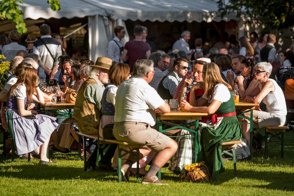 Eine Gruppe von Menschen sitzt an Tischen in einem Garten. Sie genießen das schöne Wetter und die Gesellschaft, während im Hintergrund weitere Besucher zu sehen sind. | © Narzissenfestverein/St. Pelizzari