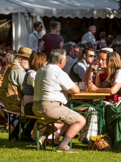 A group of people is sitting at tables in a garden. They are enjoying the nice weather and each other's company, while in the background more visitors can be seen. | © Narzissenfestverein/St. Pelizzari