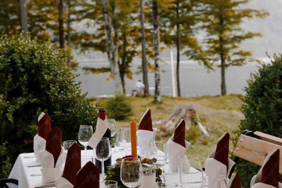 Ein schön gedeckter Tisch im Freien, umgeben von Bäumen und einer ruhigen Wasseroberfläche. Die Atmosphäre vermittelt eine gemütliche und einladende Stimmung. | © Prommer