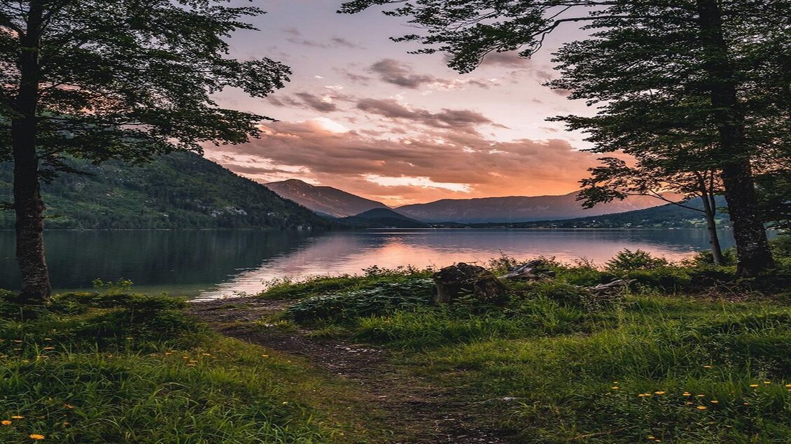 Ein ruhiger See umgeben von Bergen und Bäumen. Der Himmel ist in sanften Farben bei Sonnenuntergang getaucht. | © Peter Prommer