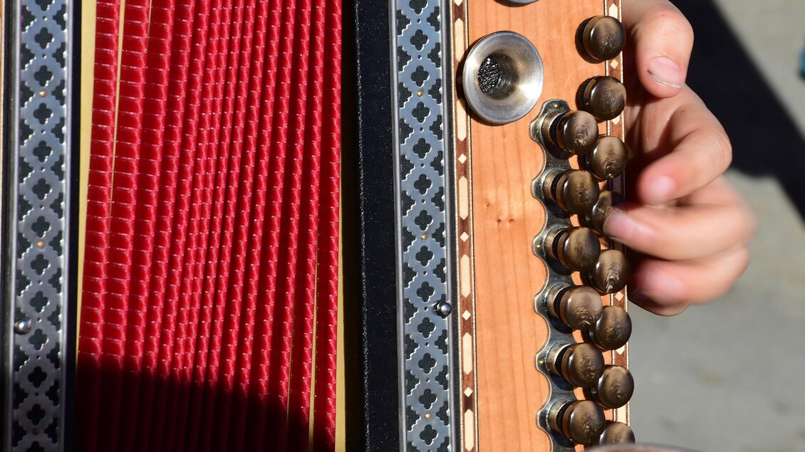 Ein Musiker spielt ein Akkordeon mit rotem Innenleben. Die Hand drückt die Tasten und erzeugt musikalische Klänge. | © (c) Wolfgang Spitzbar