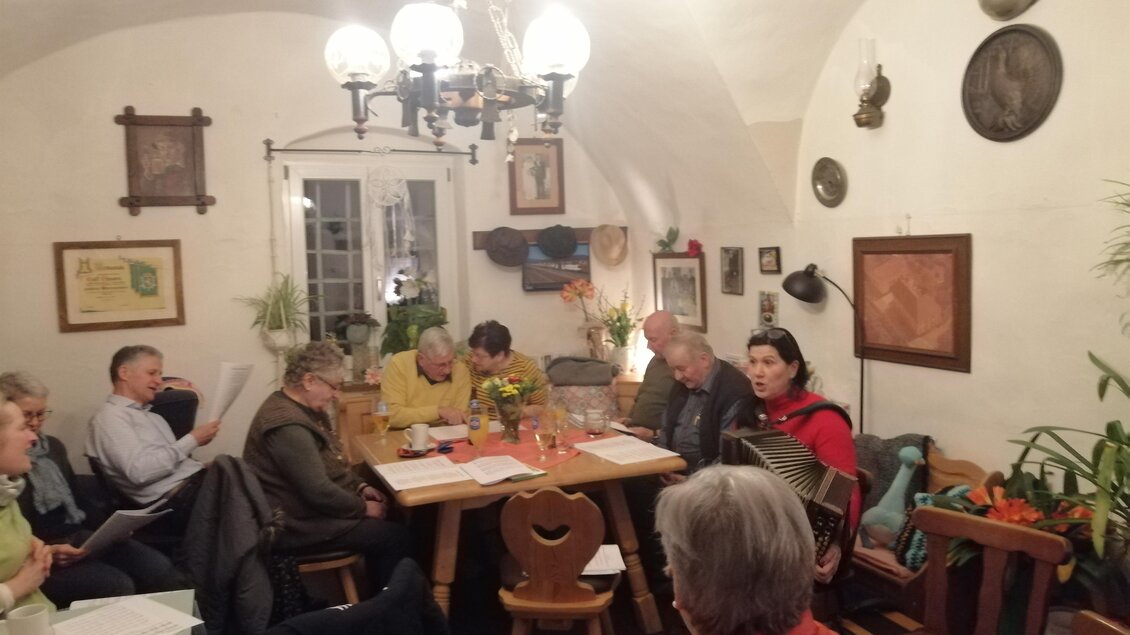 Eine Gruppe von Menschen sitzt an einem Tisch in einem gemütlichen Raum. An den Wänden hängen verschiedene Bilder und es gibt Pflanzen im Hintergrund. | © Christa Ortner