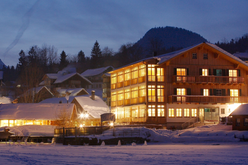 Ein schönes Gebäude im Schnee erleuchtet von warmem Licht. Im Hintergrund sind bewaldete Hügel und ein klarer Abendhimmel zu sehen. | © Seehotel Grundlsee