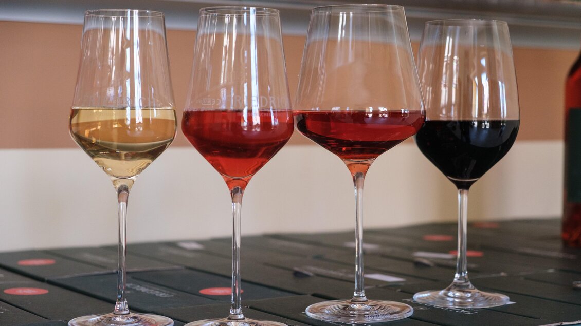 Vier Weingläser mit verschiedenen Weinsorten stehen auf einer Tischfläche. Die Gläser enthalten Weißwein, Rosé, Rotwein und einen dunklen Rotwein. | © CDM