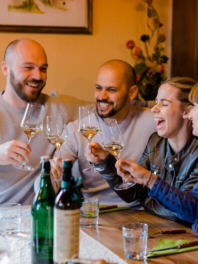 Eine fröhliche Gruppe von Freunden hebt ihre Weingläser zum Anstoßen. Sie sitzen an einem Tisch mit Getränken und genießen eine gesellige Zeit miteinander. | © Ratscher Landhaus| Karin Bergmann