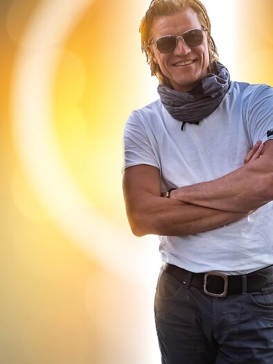 Ein lächelnder Mann mit Sonnenbrille steht mit verschränkten Armen. Er trägt ein einfaches T-Shirt und hat einen Schal um den Hals. | © geryseidl.at