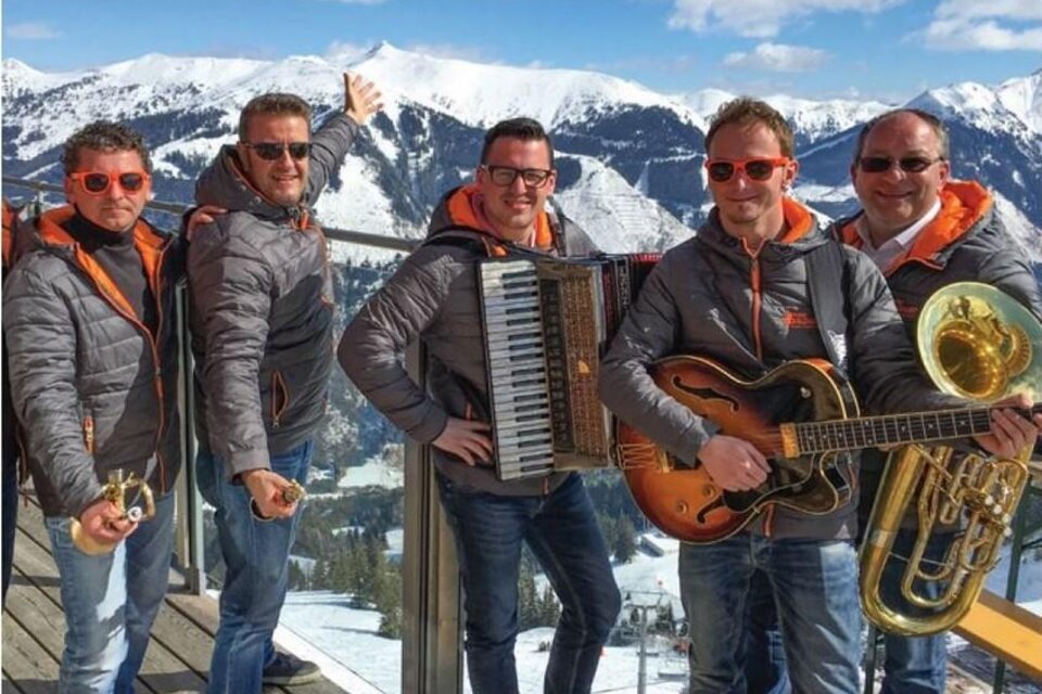 Eine Gruppe von fünf Männern in sportlichen Jacken steht in den Bergen. Sie spielen Instrumente und genießen die sonnige Winterlandschaft. | © Riesneralm