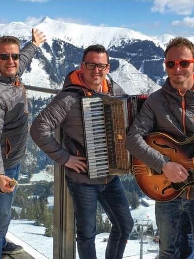 A group of five men in sporty jackets stands in the mountains. They are playing instruments and enjoying the sunny winter landscape. | © Riesneralm