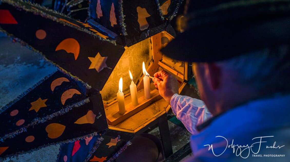 Eine Person zündet Kerzen in einer dekorativen Laterne an. Die Laterne ist mit bunten Sternen und Monden geschmückt. | © Wolfgang Fuchs