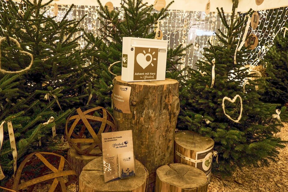 Eine festliche Weihnachtsdekoration mit Tannenbäumen, Holzscheiten und stimmungsvollem Licht. Auf einem Holzblock stehen Informationsmaterialien und liebevolle Dekorationselemente. | © Tourismusverband Oststeiermark