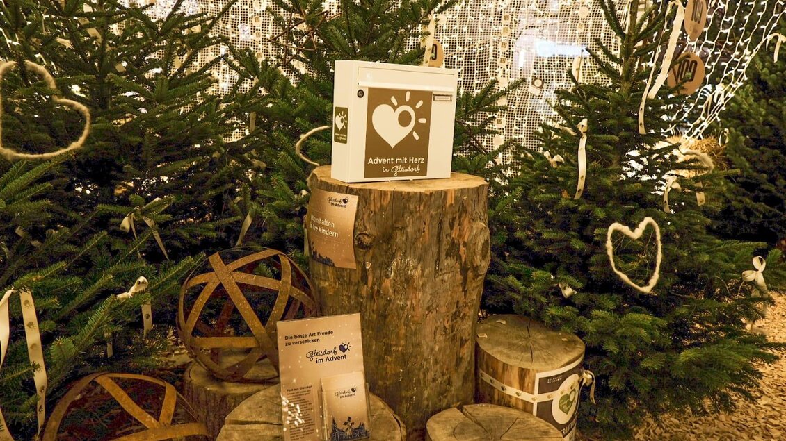 Eine festliche Weihnachtsdekoration mit Tannenbäumen, Holzscheiten und stimmungsvollem Licht. Auf einem Holzblock stehen Informationsmaterialien und liebevolle Dekorationselemente. | © Tourismusverband Oststeiermark