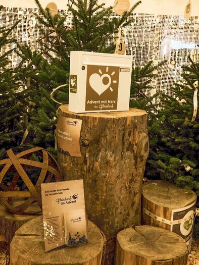 A festive Christmas decoration with Christmas trees, wooden logs, and atmospheric light. On a wooden block, there are informational materials and loving decorative elements. | © Tourismusverband Oststeiermark