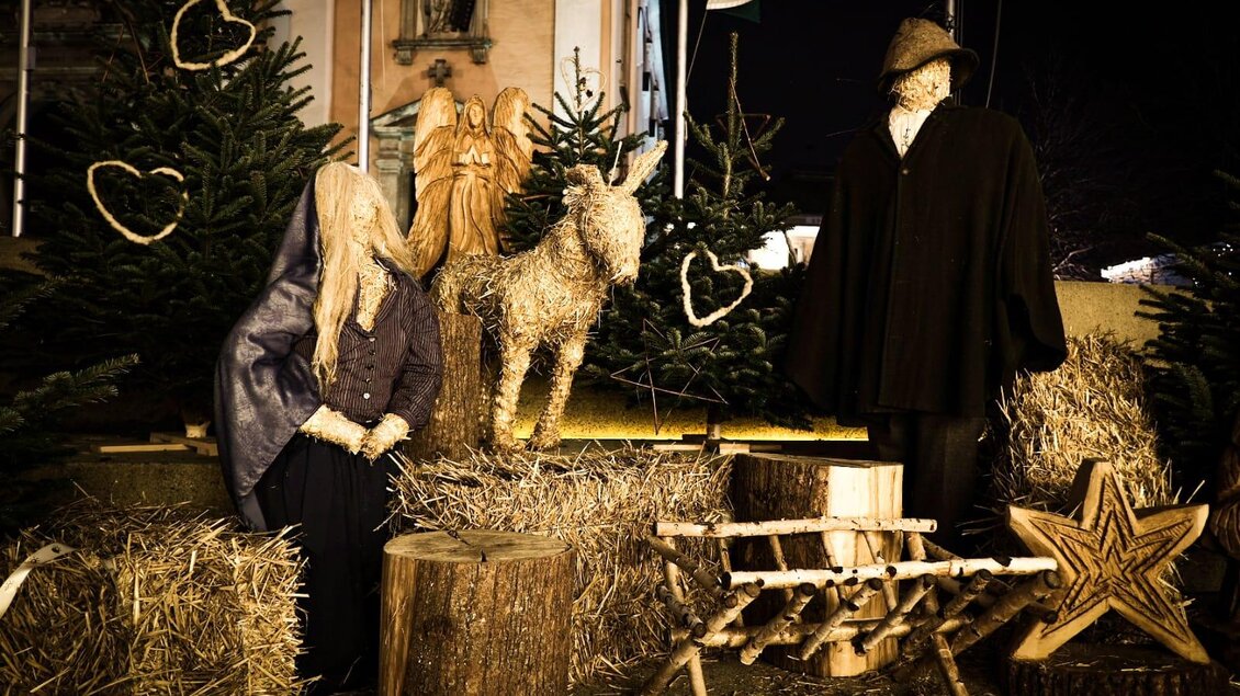 Eine festliche Weihnachtsmarktszene mit Stroh, Holzfiguren und Weihnachtsbäumen. Alte Traditionen werden durch die Darstellung einer Familie und Tiere hervorgehoben. | © Tourismusverband Oststeiermark