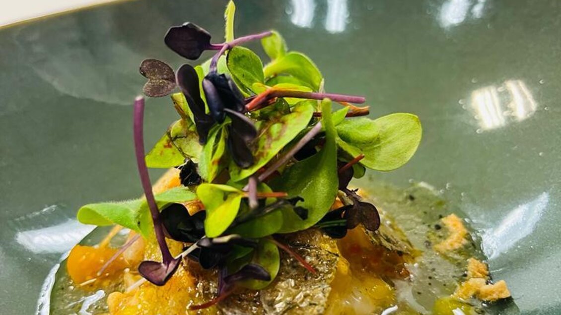 Ein kunstvoll angerichtetes Gericht auf einem grünen Teller. Es enthält eine Garnele, frische Kräuter und eine aromatische Soße. | © Andreas Wieser