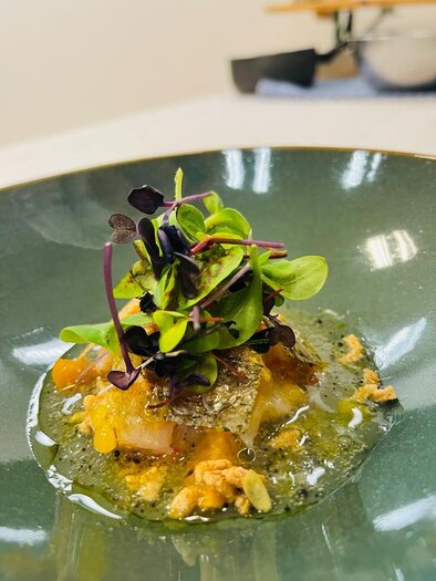 A artfully arranged dish on a green plate. It contains a shrimp, fresh herbs, and an aromatic sauce. | © Andreas Wieser