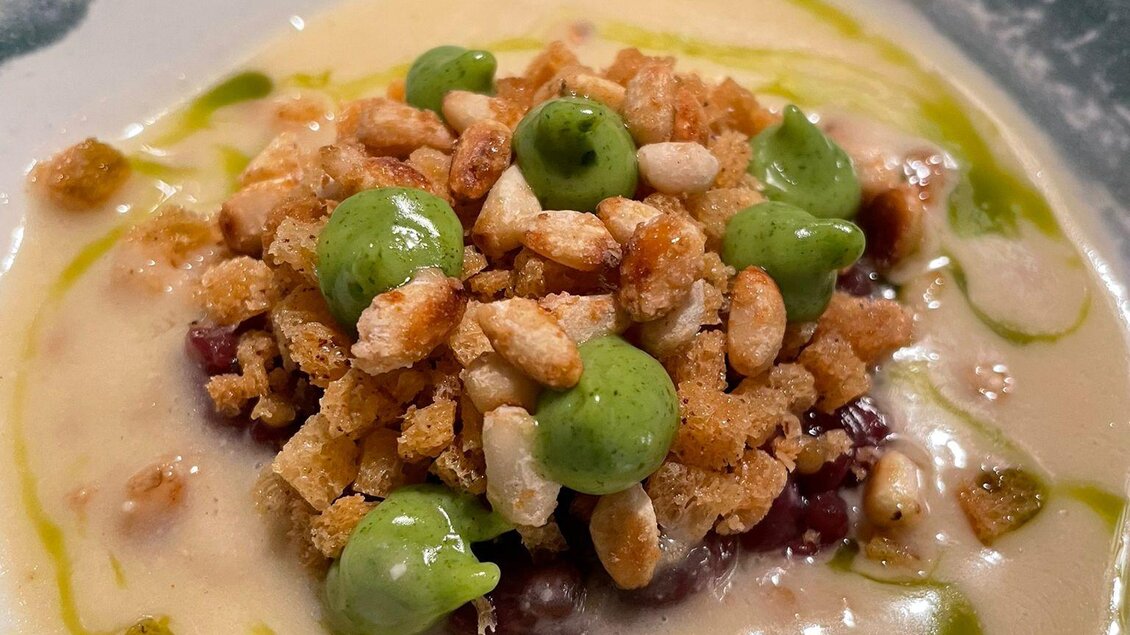 Ein kreativ angerichtetes Gericht mit einer cremigen Soße, garniert mit knusprigen Bröseln und grünen Erbsen. Es zeigt eine harmonische Kombination von Texturen und Farben. | © Andreas Wieser