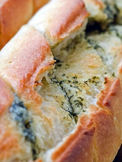 Close-up of a sliced baguette filled with herb butter. The golden brown crust and the green herbs in the cuts are clearly visible. | © Pixabay