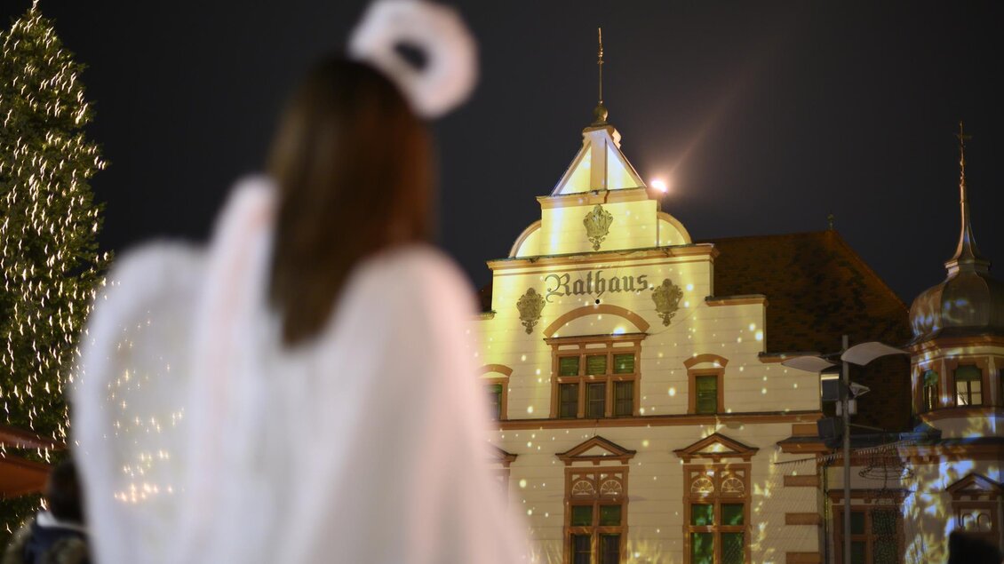 Eine Person in einem weißen Gewand steht vor einem schön dekorierten Gebäude mit festlichen Lichtern. Der Himmel ist dunkel und die Atmosphäre ist weihnachtlich. | © Tourismus Oststeiermark