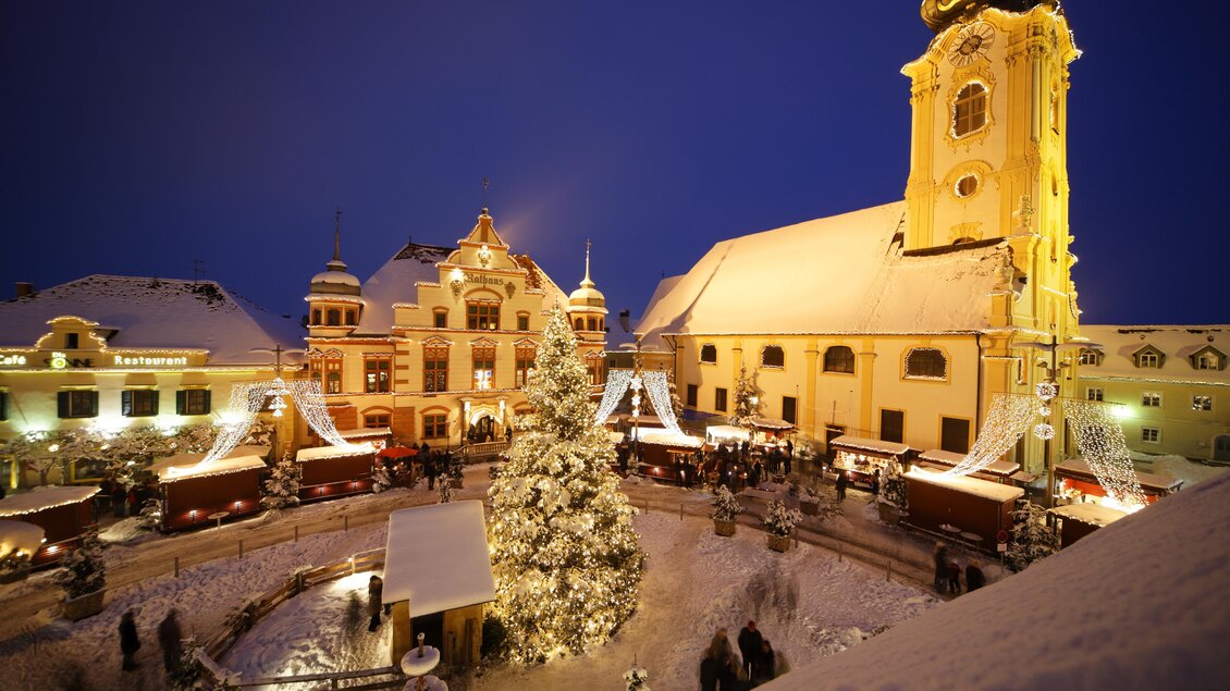 Ein festlicher Weihnachtsmarkt mit einem geschmückten Baum und bunter Beleuchtung. Die Umgebung ist mit Schnee bedeckt und die Gebäude strahlen weihnachtliche Stimmung aus. | © Bernhard Bergmann