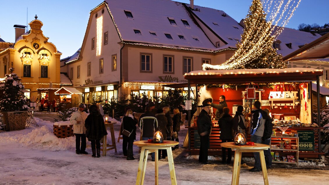 Ein winterlicher Weihnachtsmarkt mit festlich beleuchteten Ständen und Menschen, die umherwandern. Im Hintergrund sind geschmückte Gebäude unter einem klaren Himmel zu sehen. | © Bernhard Bergmann