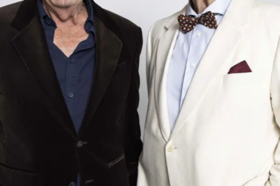 Zwei lächelnde Männer stehen nebeneinander. Der eine trägt einen schwarzen Anzug und der andere ein weißes Jackett mit einer Melone. | © Marecek&Steinhauer