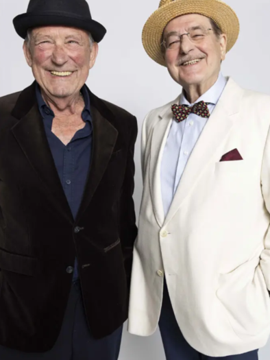 Two smiling men are standing next to each other. One is wearing a black suit and the other a white jacket with a bowler hat. | © Marecek&Steinhauer