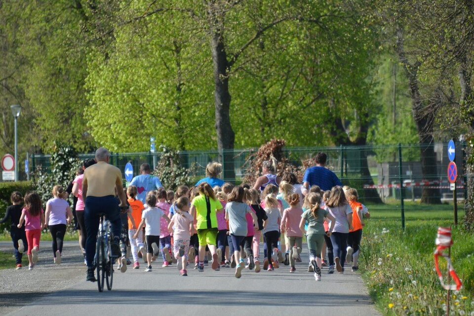 Eine Gruppe von Kindern läuft enthusiastisch auf einem Weg. Im Hintergrund fährt ein Mann auf einem Fahrrad. | © Tourismusverband Oststeiermark