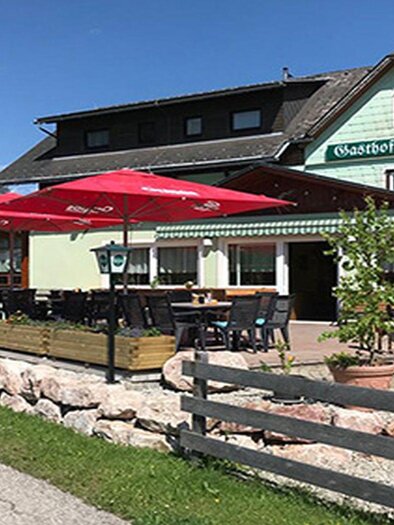 Ein Gasthof mit Außenbereich und roten Schirmen. Umgeben von Bäumen und einem gepflegten Garten. | © Gathof Moser