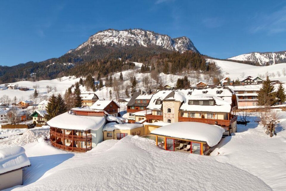 Ein malerisches Bergdorf im Winter mit schneebedeckten Häusern. Im Hintergrund erheben sich majestätische Berge unter einem klaren blauen Himmel. | © Hotel Der Hechl