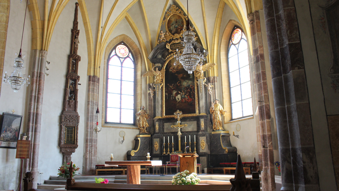 Eine Kirche mit einem eindrucksvollen Altar, Kronleuchtern und hohen, bunten Fenstern. Die Holzbänke laden zur Besinnung ein. | © Tourismusverband/Lechner Viola