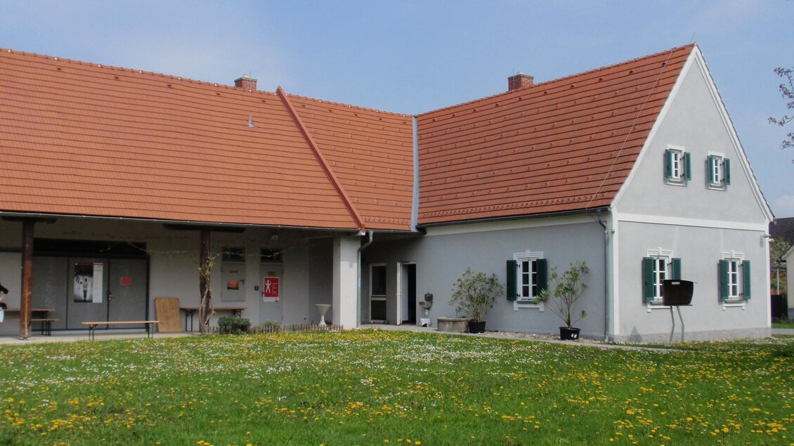 Ein charmantes Haus mit rotem Ziegeldach und weißen Wänden. Der Garten ist mit Gräsern und Löwenzahn bewachsen. | © David Kranzelbinder
