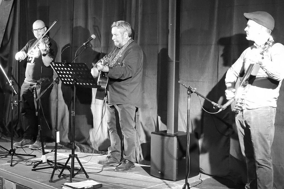 Drei Musiker stehen auf einer Bühne und spielen live Musik. Einer spielt Geige, während die anderen Gitarre spielen und singen. | © Stadtgemeinde Trofaiach