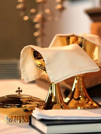 A table with golden cutlery, a jug, and a book. On it lie napkins and decorative elements. | © Tieber Doris