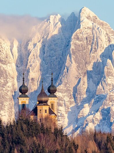 Eine malerische Kirche vor majestätischen, schneebedeckten Bergen. Der Himmel ist klar und die Landschaft wirkt friedlich.