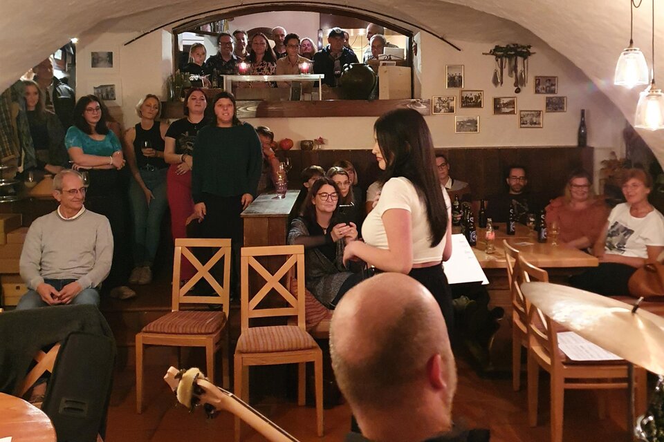 Eine lebhafte Veranstaltung in einem gemütlichen Kellerlokal. Menschen stehen und sitzen, um einen Auftritt zu genießen. | © Sabine Hermann