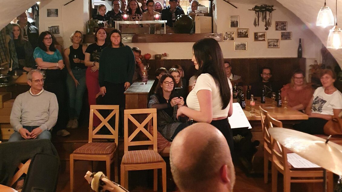 Eine lebhafte Veranstaltung in einem gemütlichen Kellerlokal. Menschen stehen und sitzen, um einen Auftritt zu genießen. | © Sabine Hermann