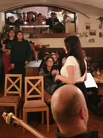 Eine lebhafte Veranstaltung in einem gemütlichen Kellerlokal. Menschen stehen und sitzen, um einen Auftritt zu genießen. | © Sabine Hermann