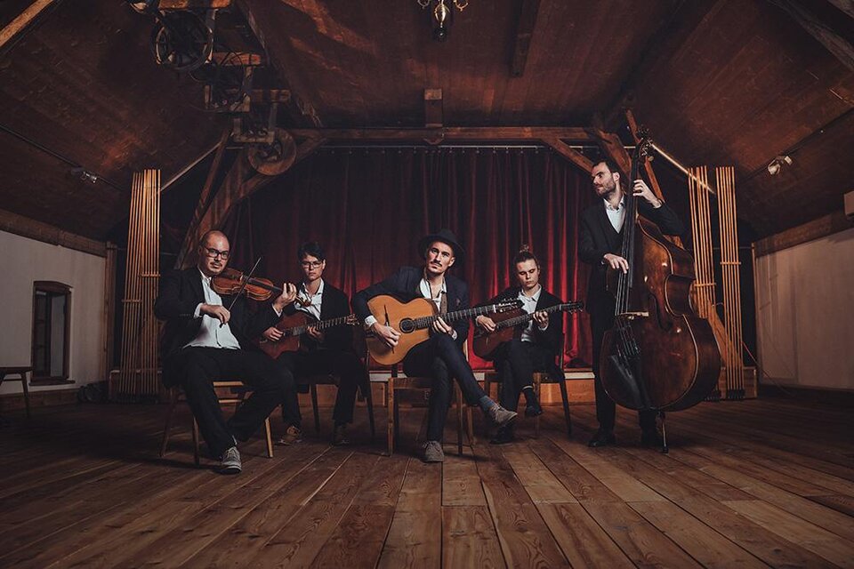 Eine Band tritt in einem rustikalen Raum mit Holzboden auf. Sie spielen verschiedene Instrumente, darunter Gitarre, Violine und Kontrabass. | ©  Reithofer Media