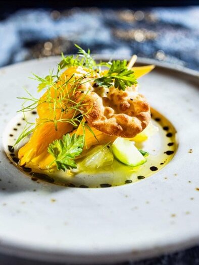 An artfully arranged dish on a white plate. It consists of fresh ingredients, including orange elements and herbs. | © Der Thaller