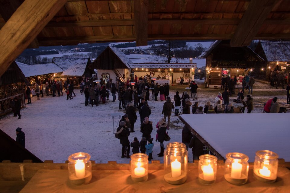 Ein festlicher Weihnachtsmarkt bei Nacht, beleuchtet von Kerzen und Lichtern. Menschen schlendern zwischen den Ständen und genießen die gemütliche Atmosphäre. | © Klaudia Riebenbauer