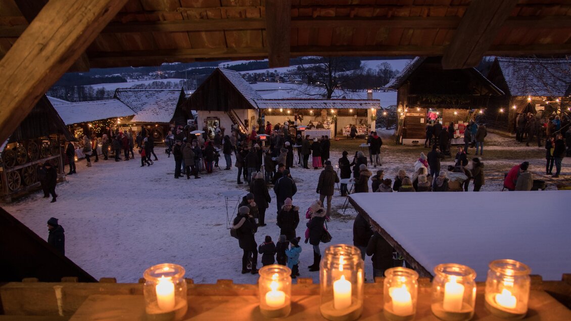 Ein festlicher Weihnachtsmarkt bei Nacht, beleuchtet von Kerzen und Lichtern. Menschen schlendern zwischen den Ständen und genießen die gemütliche Atmosphäre. | © Klaudia Riebenbauer