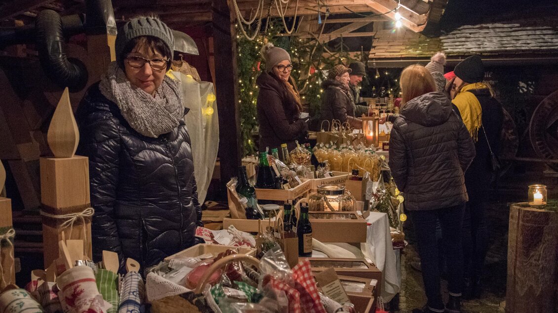 Ein winterlicher Markt mit Ständen voller Geschenke und Getränken. Menschen genießen die festliche Atmosphäre bei gedämpftem Licht. | © Klaudia Riebenbauer