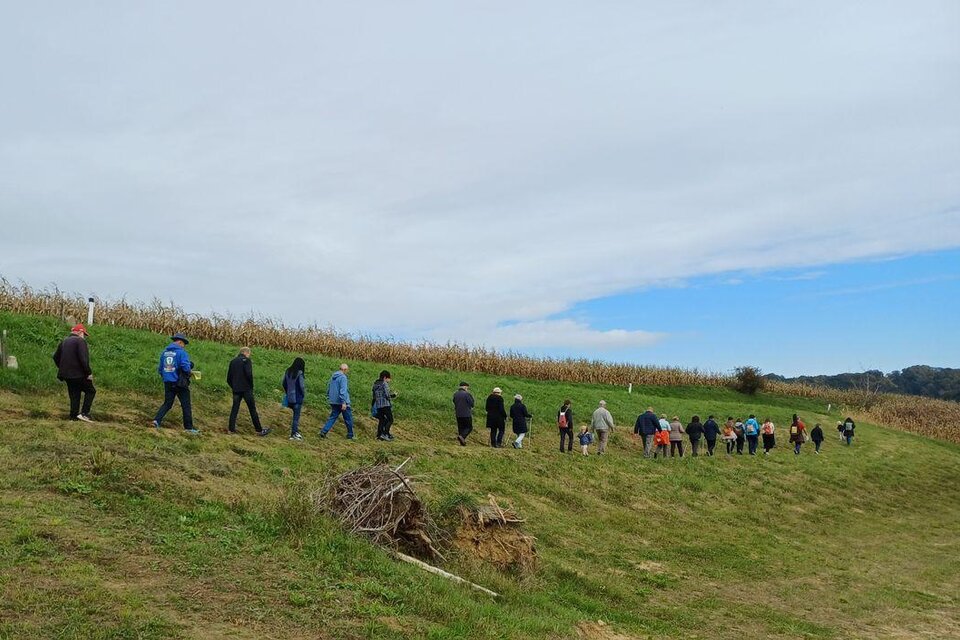 Eine Gruppe von Menschen wandert auf einem Weg entlang eines Feldes. Der Himmel ist teilweise bewölkt und die Landschaft ist grün. | © Anna Maria Ladler