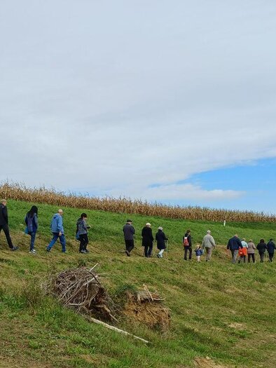 Eine Gruppe von Menschen wandert auf einem Weg entlang eines Feldes. Der Himmel ist teilweise bewölkt und die Landschaft ist grün. | © Anna Maria Ladler