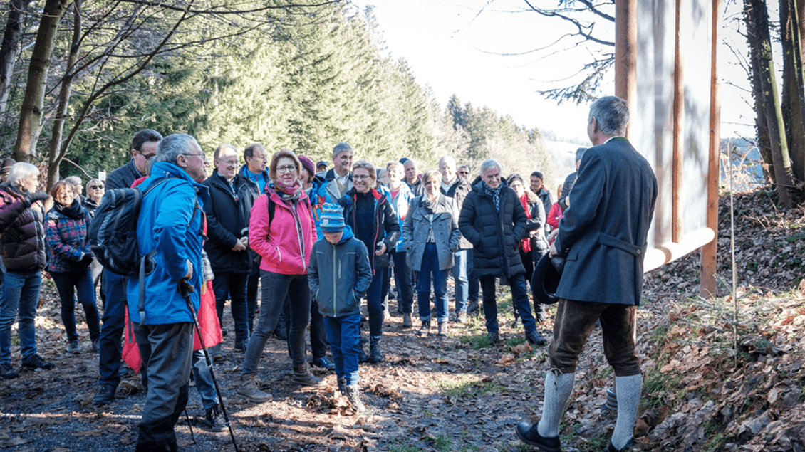 Eine Gruppe von Menschen hört einem Redner im Wald aufmerksam zu. Es ist ein sonniger Tag und die Umgebung ist von Bäumen umgeben. | © Florian Jöbstl