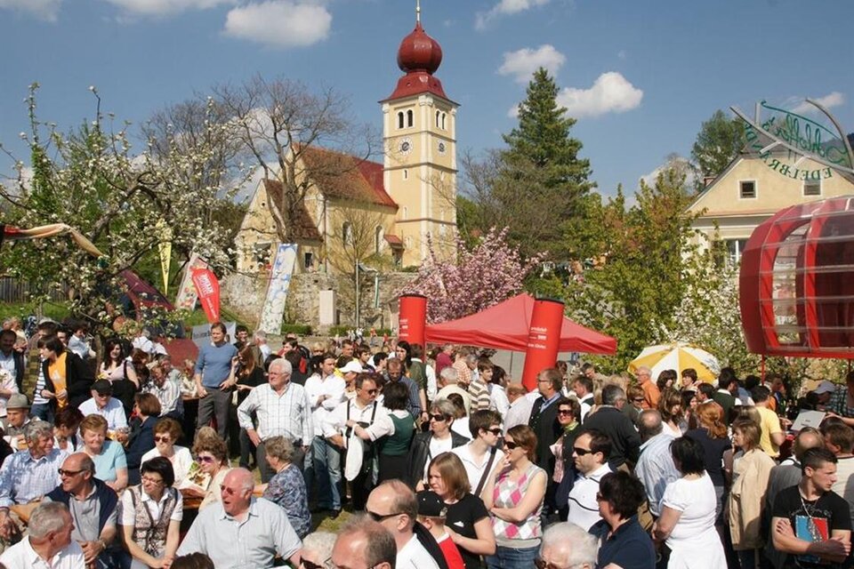 Ein lebhaftes Fest mit vielen Menschen, die zusammen feiern. Im Hintergrund sieht man eine historische Kirche und blühende Bäume. | © Tourismusverband Oststeiermark/Walter Schneider