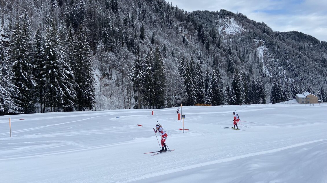 Zwei Skifahrer auf einer verschneiten Piste in einer malerischen Berglandschaft. Hohe Tannenbäume und schneebedeckte Hügel umgeben die Szene. | © NAZ Eisenerz