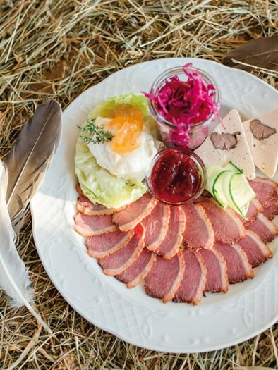 A plate with various meat specialties, salad, and jam. The plate is placed on a bed of hay. | © Buschenschank Tinnauer